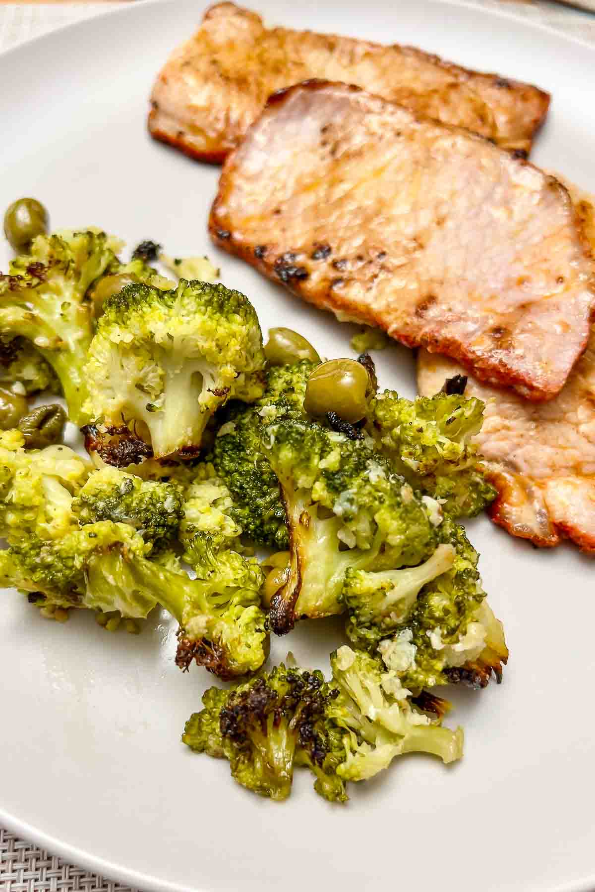 Pork loin in adobe spanish style served with roasted broccoli and olives on a white plate.