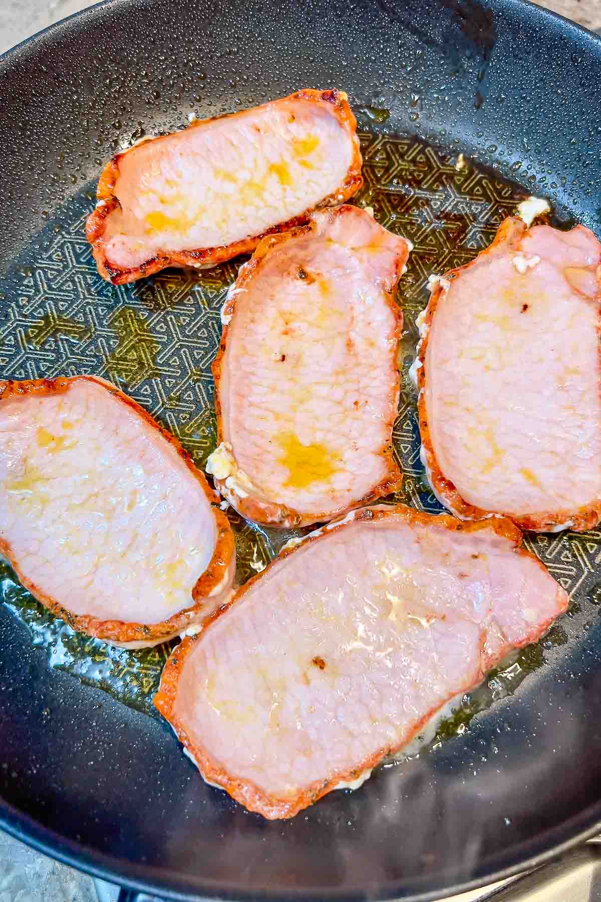 slices of pork loin in adobo cooking in olive oil in a pan.