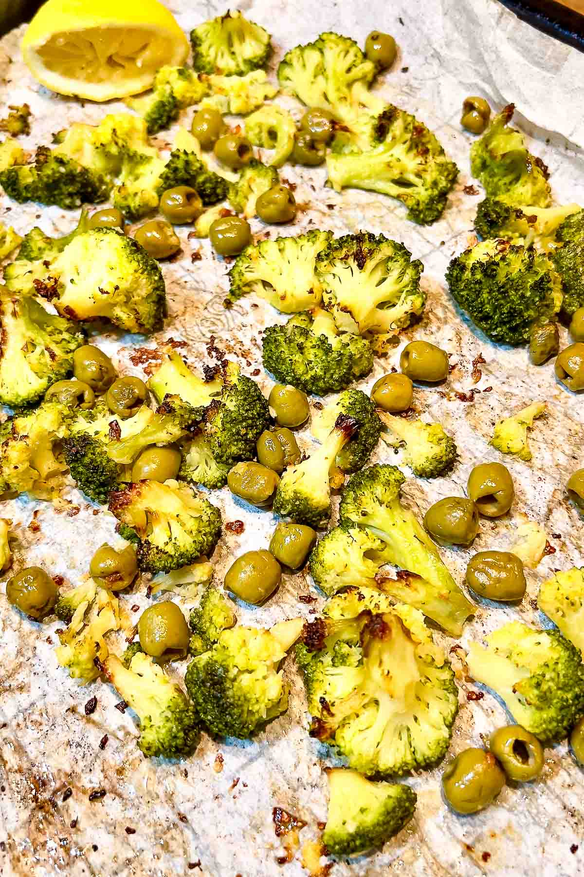Roasted broccoli and olives on a baking sheet.